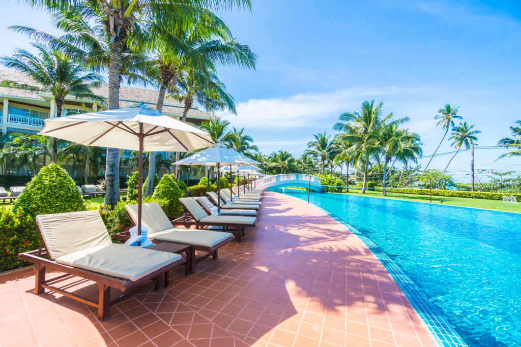 Beautiful luxury umbrella and chair around outdoor swimming pool in hotel and resort with coconut palm tree on blue sky - Boost up color Processing